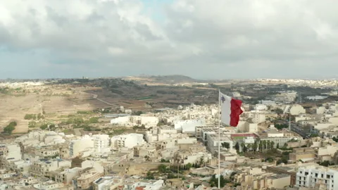 Flag of Malta waving in Wind with view of City on Gozo Island, Aerial Close up Vidéo 141259745