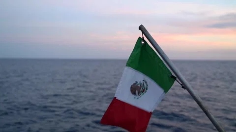 Flag of Mexico rippling off the back of a boat over the ocean during sunset Stock Footage 248477267