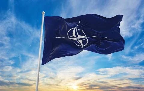 Flag of NATO waving in the wind on flagpole against the sky with clouds on su Stock Illustration