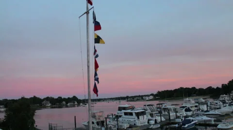Flag pole over looking a boat harbor at dusk Stock Footage 28047762