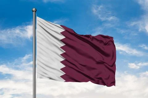 Flag of Qatar waving in the wind against white cloudy blue sky. Qatari flag. Stock Photos