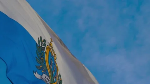 The Flag of San Marino Billows in the Wind Against a Blue Sky, HD Stock Footage 220428398