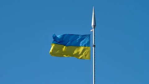 The flag of Ukraine flutters on a flagpole, during the day against a blue sky. Stock Footage 241134697