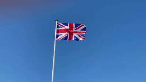 Flag of United Kingdom is waving in the wind. Bright sunny day, blue sky Stock Footage 134353586