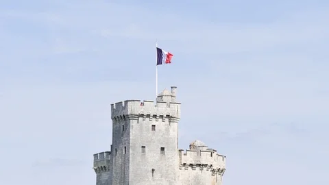 A flag in the wind, above a tower in La Rochelle, a city in western France. Stock Footage 94825999