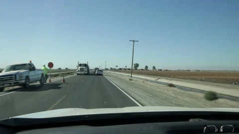 A Flagman controls traffic on a rural road in Merced County California Stock Footage 163239088