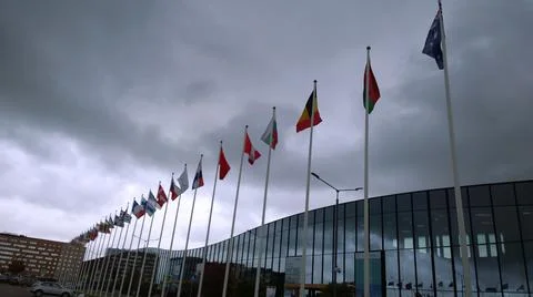 Flags of different countries on flagpoles against dark overcast sky Stock Photos