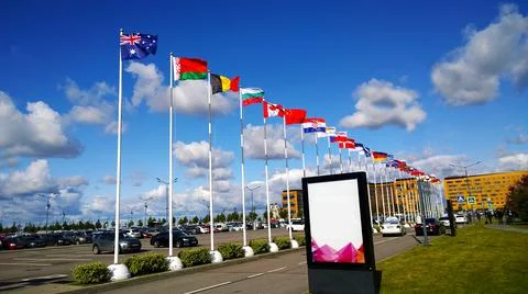 Flags of different countries on flagpoles against blue sky near International Stock Photos