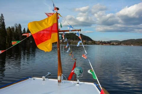 Flags from different countries on a ship in front of a town on Lake Titisee Stock Photos