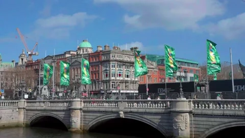 Flags wave in the breeze on O'Connell Bridge, with bustling crowds and historic Stock Footage 334685222