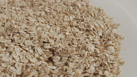 Flakes of oat fall on plate pile 4K video Stock Footage 179999549