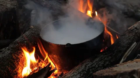 Flame around the pot. in the evening to cook on the fire. in a pot standing on Stock Footage 77504487