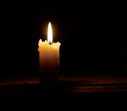 The flame of a burning candle in the dark. A single lit, melted candle on a b Foto stock