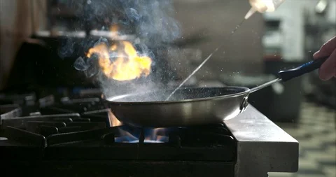 Flame erupts in a hot kitchen and butter is being poured into a red hot pan Stock Footage 105376889