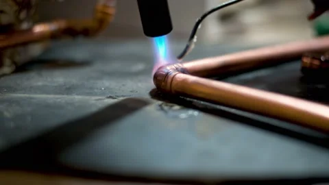 Flame from a gas blowtorch being applied to a copper pipe fitting, to melt Stock Footage 148952424