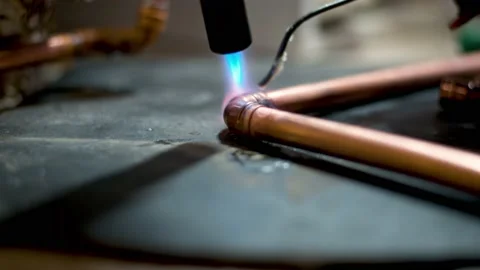 Flame from a gas blowtorch being applied to a copper pipe fitting, to melt Stock Footage 148998619