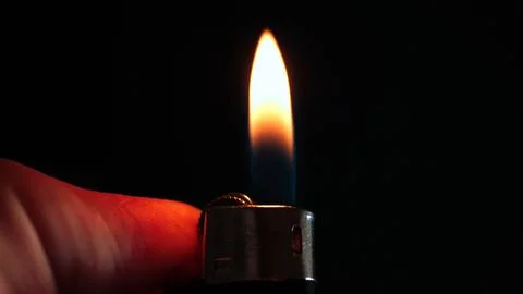 The flame of a lighter on a dark background is a close-up. Red light from a Stock Photos