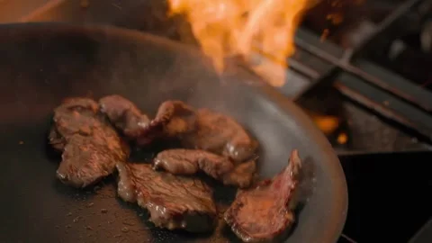 Flame sears raw beef slices in pan on professional gas stove Stock Footage 313031825