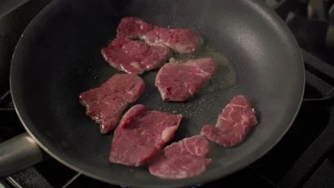 Flame sears raw beef slices in pan on professional gas stove Stock Footage 313031860