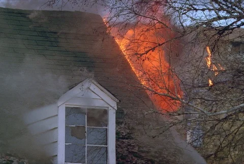 Flames and smoke roll upward from the roof of a burning house. Twigs on a tree Stock Footage 86774168