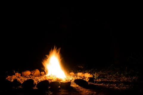 Flames of a campfire in deep darkness surrounded by stones shaping strong Stock Photos