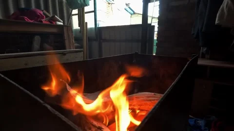 Flames dance and flicker in a metal fire pit, illuminating the warm glow of Stock Footage 334738778