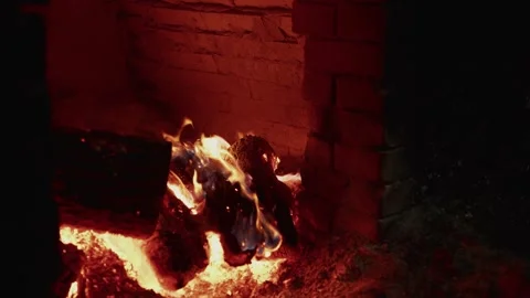 Flames dance around burning logs in a rustic fireplace, illuminating the brick Vídeo Stock 332724207