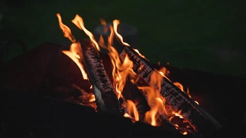 Flames dance around several logs in a fire pit as they burn brightly. The bright Video stock 345874579