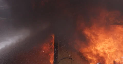 Flames devour a corner of a burning structure as spray from fire hoses comes in Stock Footage 59534693