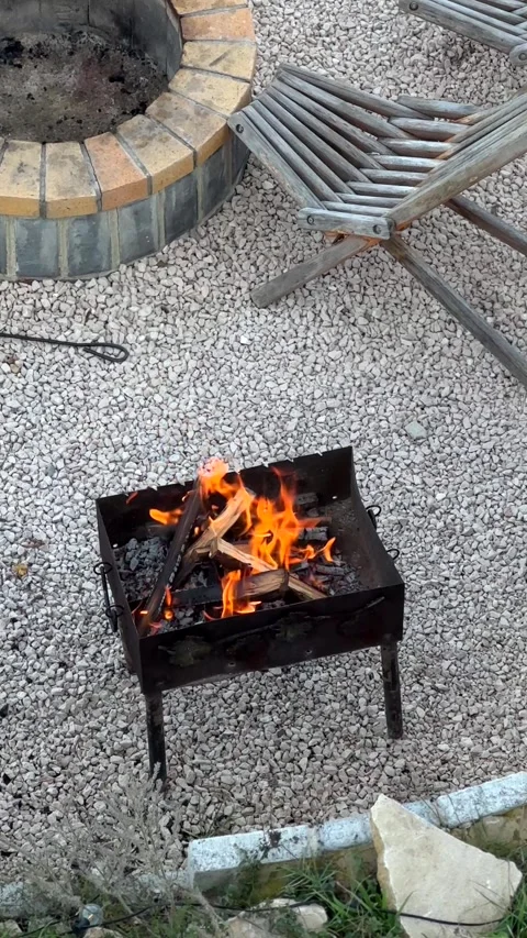 Flames flicker above burning wood in barbecue surrounded by gravel Stock Footage 340382403