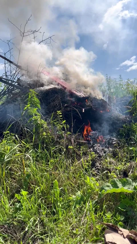 Flames flicker and smoke rises from a burning debris pile Stock Footage 316475102