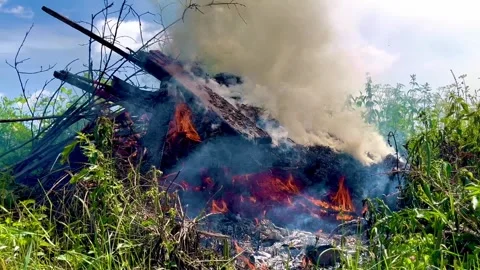 Flames flicker and smoke rises from a burning debris pile Stock Footage 319299410