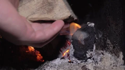 Flames flicker as hand adds kindling to burning logs in a fireplace, smoke Stock Footage 327916147