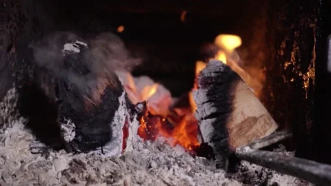 Flames flicker as a metal rod stirs glowing embers and logs in a fireplace, Stock Footage 335241532
