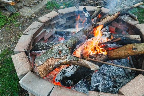 Flames rise from a fire pit made of stone. Logs and branches are burning, and Fotos Stock