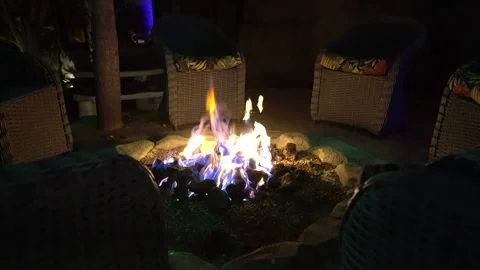 Flames in a stone fire pit seen between wicker chairs at night Stock Footage 345540607