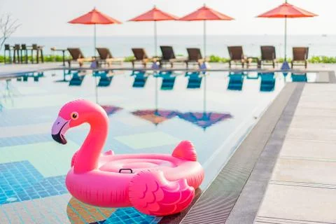 Flamingo float around swimming pool in hotel resort with umbrella and chair i 写真素材