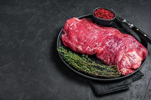 Flank or flap raw beef steak on plate with thyme. Black background. Top view Stock Photos