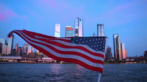 Flapping American flag set against the waterscape and city skyline. Skyscrapers Stock Footage 329191975