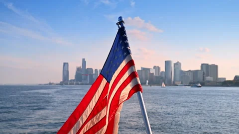 Flapping flag of America at the backdrop of riverscape. Hazy New York skyline at Stock Footage 316557029