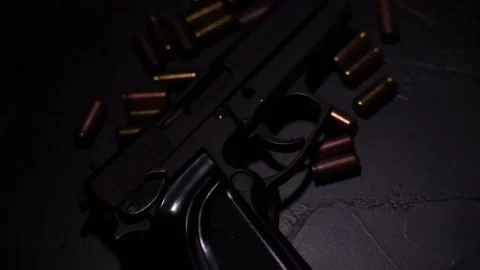 Flashlight illuminates hand gun and bullets on black concrete table. Video stock 146183917