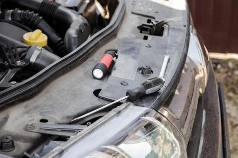 Flashlight, screwdriver and key lie on the open hood of the car Stock Photos