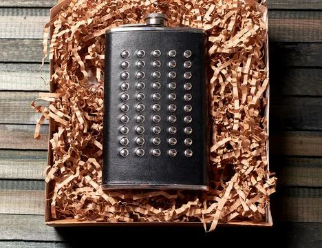 A flask in a black leather case with rivets. A gift in a brown h Stock Photos