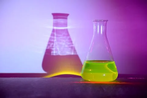 A flask with glowing green liquid casting colorful shadows Stock Photos