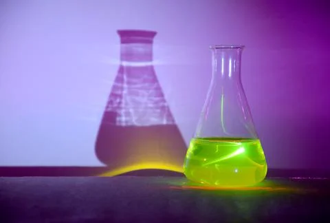 A flask with glowing green liquid casting colorful shadows Stock Photos
