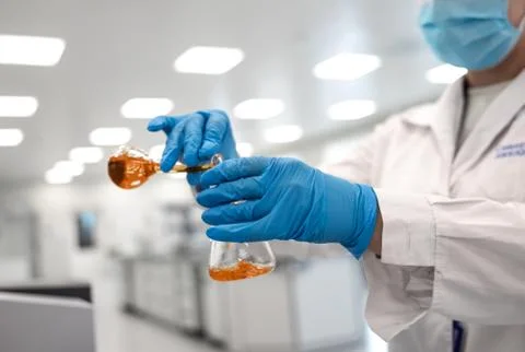 Flasks with brown liquid in scientist hands with dropping chemical liquid to Fotos Stock
