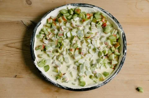 Flat baking pan with uncooked pie dough green rhubarb pieces in sauce on table Stock Photos