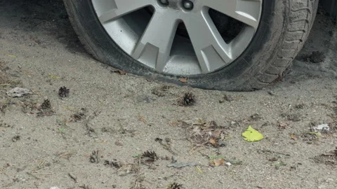 Flat car tire and wheel rim on dusty gravel ground with dirt buildup and visible Stock Footage 345765642