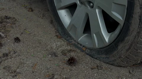 Flat car tire with damaged sidewall resting on gravel beside vehicle wheel and Stock Footage 345765460