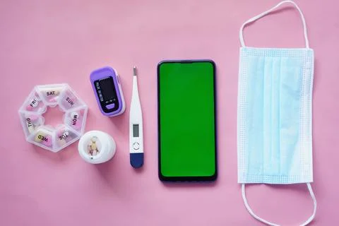 Flat composition of smart phone, mask, thermometer and sanitizer on pink Stock Photos
